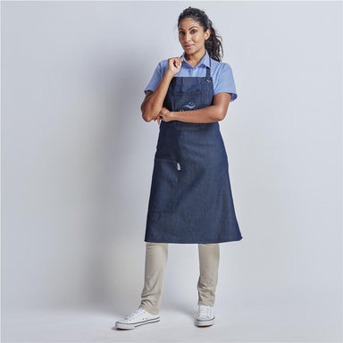 Woman wearing a blue apron over a light blue shirt and beige pants on a white background