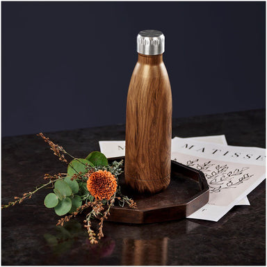 Wooden water bottle with silver cap on a dark surface with flowers and paper.
